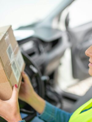 A woman courier checks a delivery package while seated inside a car, ready for distribution.