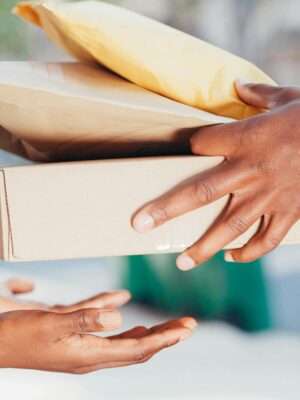 Close-up image of hands exchanging packages outdoors. Represents delivery and shipping services.