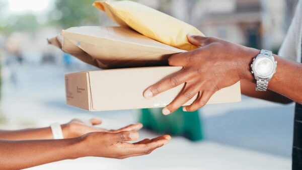 Close-up image of hands exchanging packages outdoors. Represents delivery and shipping services.