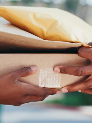 Close-up of hands exchanging a parcel and envelope outdoors, showcasing delivery service.