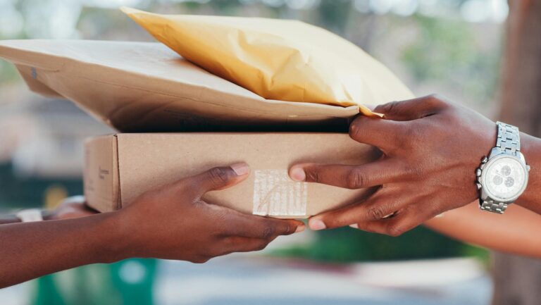 Close-up of hands exchanging a parcel and envelope outdoors, showcasing delivery service.