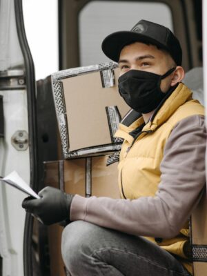 Courier wearing face mask delivers packages, seated in a van. New normal logistics service.