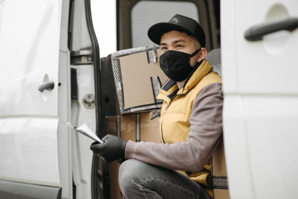 Courier wearing face mask delivers packages, seated in a van. New normal logistics service.