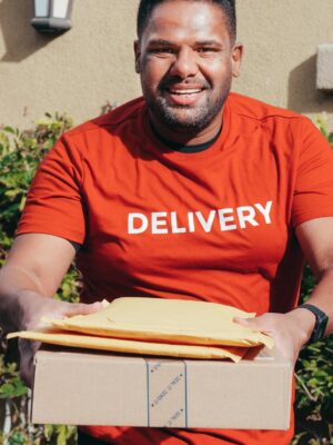 Smiling delivery man in red shirt holding packages, standing outdoors. Perfect for e-commerce and logistics concepts.