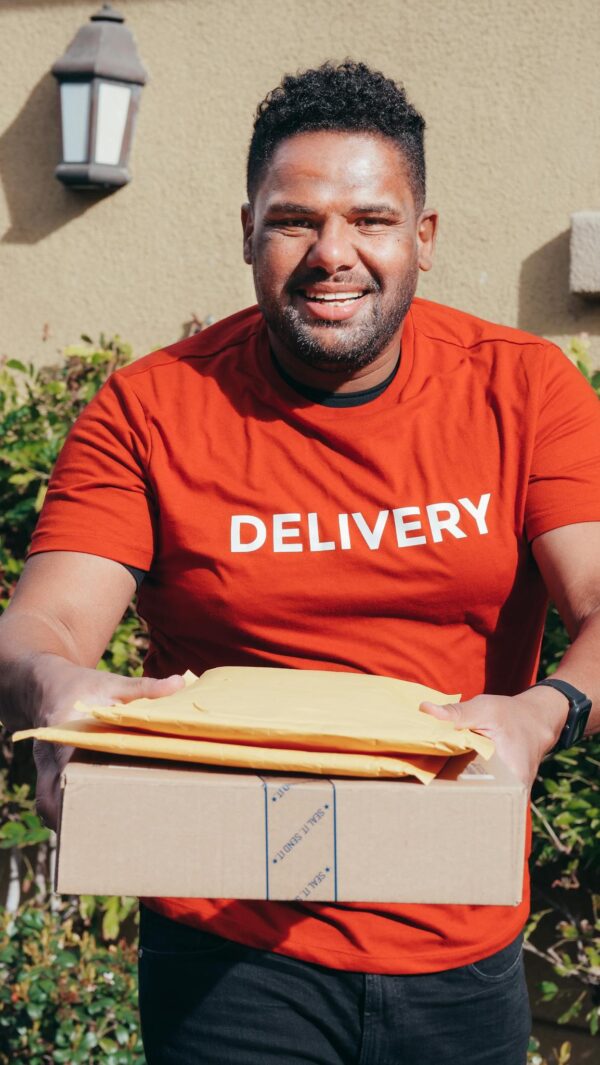 Smiling delivery man in red shirt holding packages, standing outdoors. Perfect for e-commerce and logistics concepts.